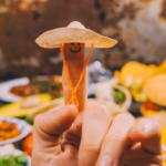finger with smiley wearing a Mexican hat with blurred Mexican food in the background.