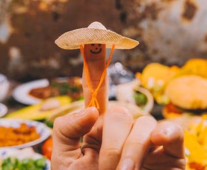 finger with smiley wearing a Mexican hat with blurred Mexican food in the background.