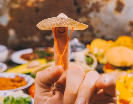 finger with smiley wearing a Mexican hat with blurred Mexican food in the background.